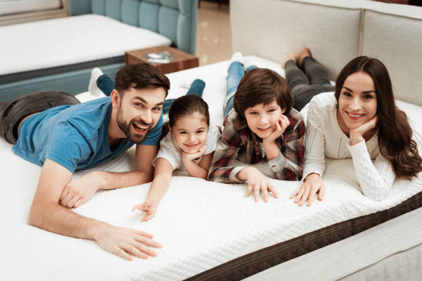 Happy family is relaxing on mattress in orthopedic furniture store. Big family check softness of mattress stock photo