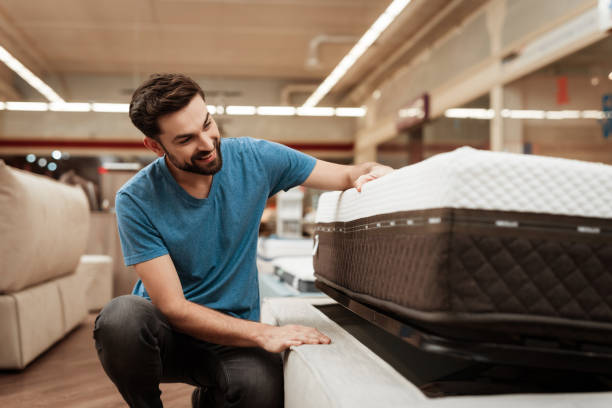 Young bearded man is testing mattress in furniture store. Orthopedic mattress for a healthy posture. stock photo