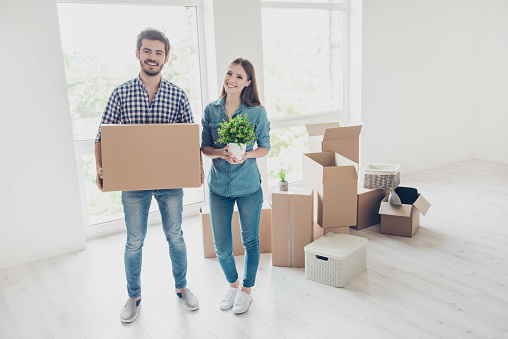 New life, new start, new home for a young family. What a joy! Happy cheerful lovers are unpacking in a new apartment, standing in a casual wear