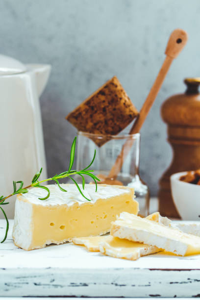 istock Cheese plate served with crackers, honey and nuts. Camembert on white wood serving board over white texture background. Appetizer theme. 939653938