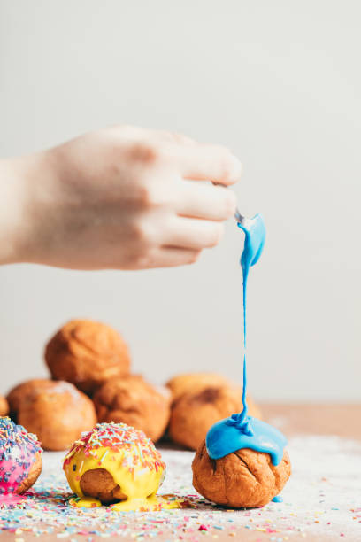 istock Woman's hand coating a doughnut with blue frosting. 939658702