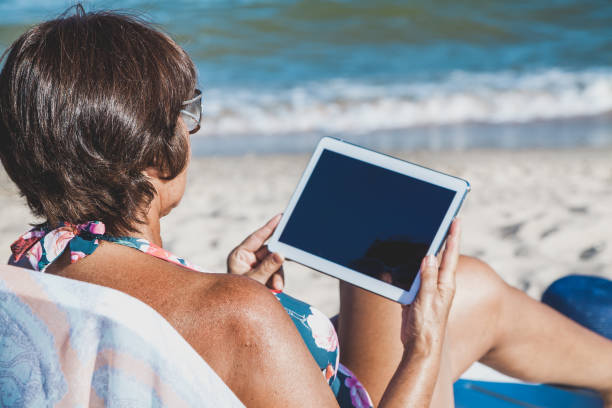 istock Elderly woman with tablet on beach 939659174