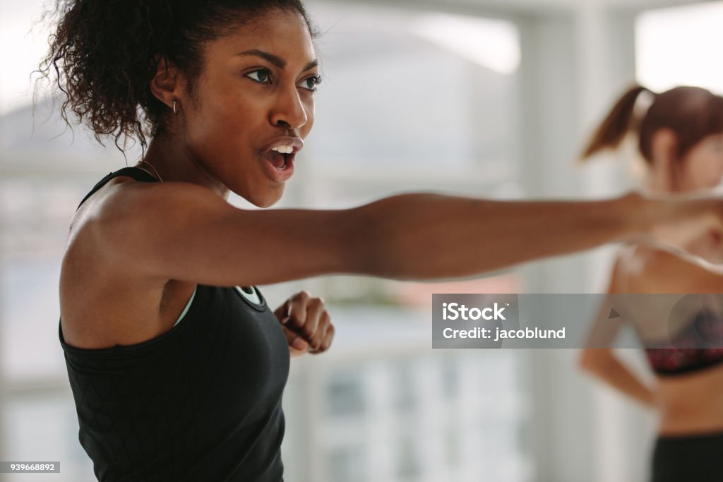 Women doing intense punching work out at the gym African young woman doing intense punching work out at the gym. Young slim woman in sportswear doing exercise during intensive circuit training. Exercising Stock Photo