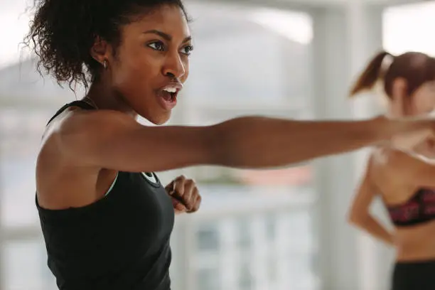African young woman doing intense punching work out at the gym. Young slim woman in sportswear doing exercise during intensive circuit training.