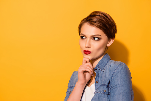 Close up portrait of minded attractive young lady with red lipd dressed in jeans shirt thinking about what to choose