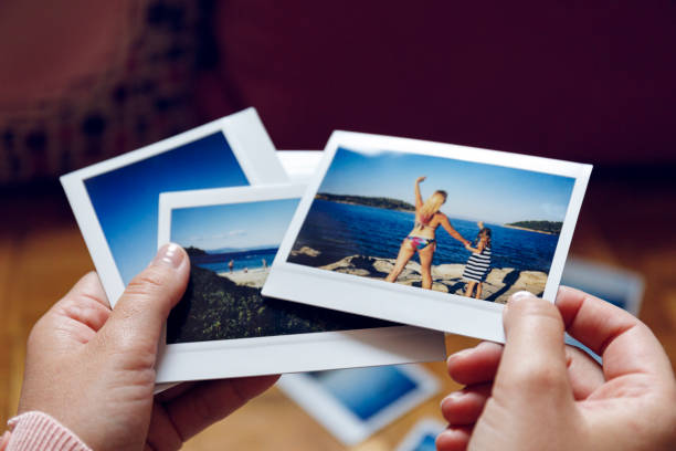 Browsing vacation photographs at home - a closeup Young woman is browsing polaroid images from yesteryear summer vacation she spent with family in Greece. Authentic moments, original photographs. holding hands photos stock pictures, royalty-free photos & images