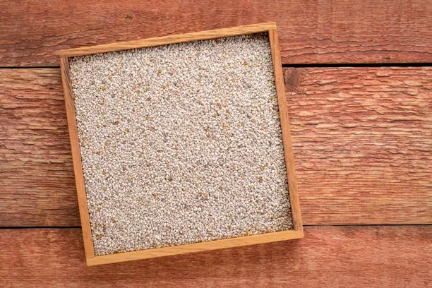 organic white chia seeds in a wooden box against weather wood background with a copy space