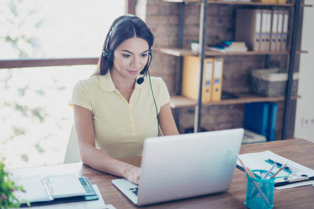 successful young latin girl is talking to customer with headset on and putting data in her computer - speech recruitment technology young adult imagens e fotografias de stock