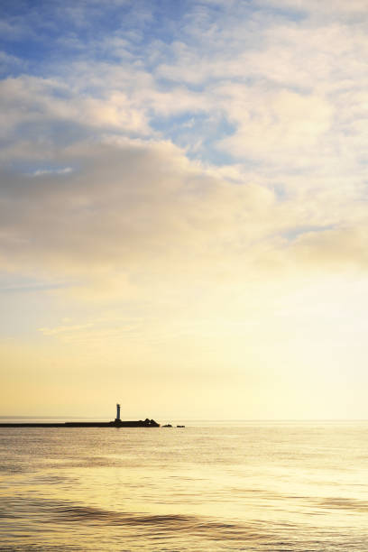 Vertical image of a distant lighthouse silhouette on a stone pier on daugava river in Riga at sunset