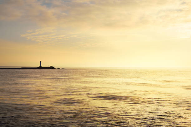 istock Horizontal image of a distant lighthouse silhouette on a stone pier on daugava river in Riga at sunset 939679590