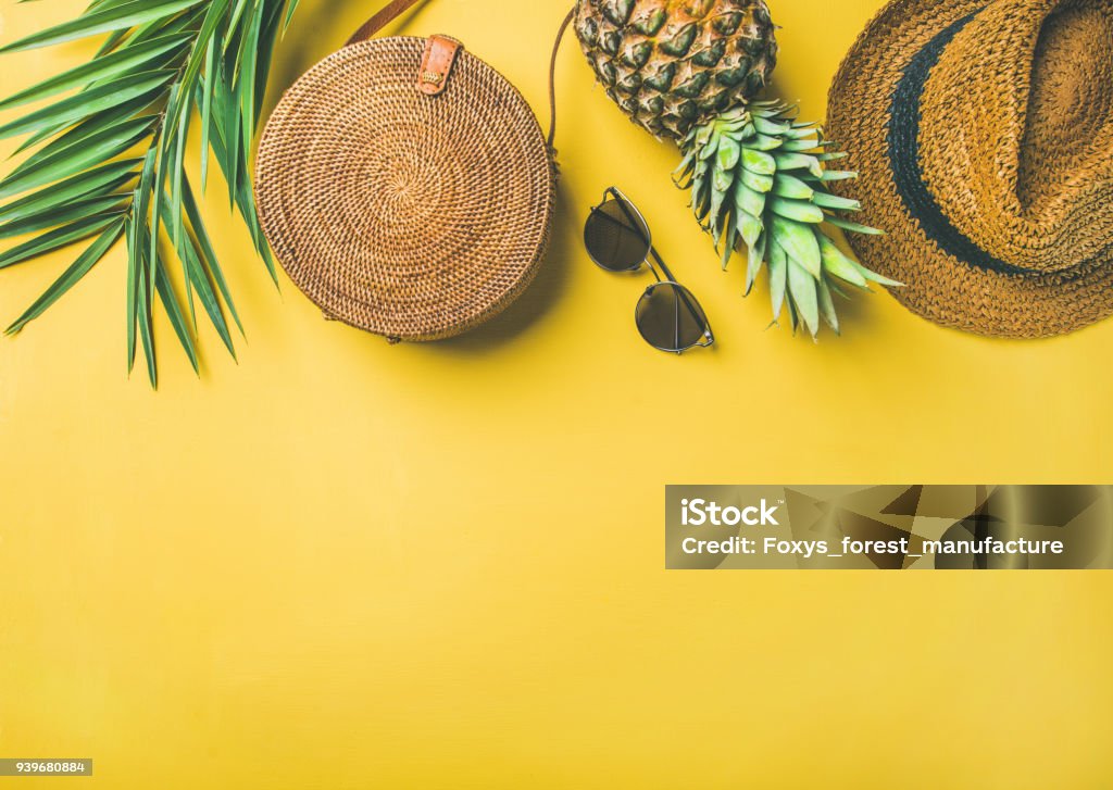 Colorful summer female fashion outfit over yellow background Colorful summer female fashion outfit flat-lay. Straw hat, bamboo bag, sunglasses, palm branches, fresh pineapple over yellow background, top view, copy space. Summer fashion, holiday travel concept Sunglasses Stock Photo