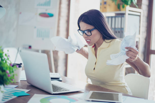 mal humor. empresaria joven enojado es ropa casual y gafas está cansado de su trabajo en la oficina, arruguen papeles y gritando en el portátil - crumpled paper document frustration fotografías e imágenes de stock