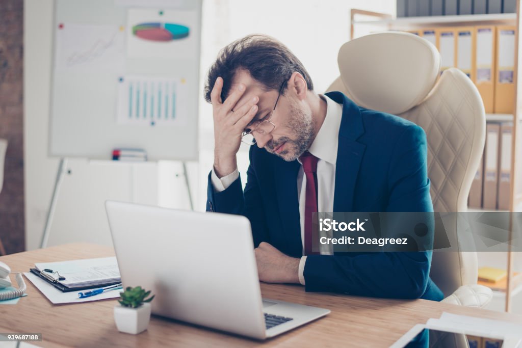 Agent immobilier déprimé entrepreneur tient sa tête avec la main, il est fatigué et frustré, assis dans le Bureau sur son lieu de travail - Photo de Stress libre de droits