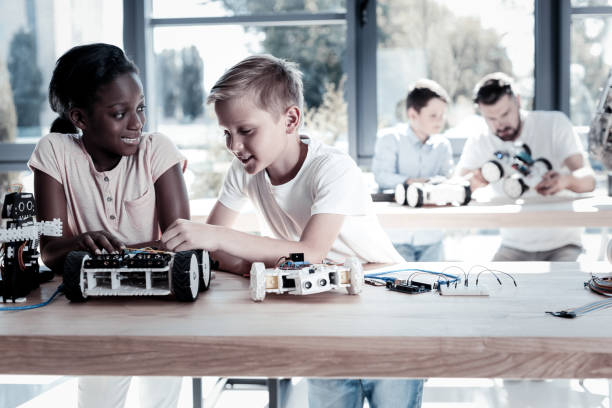 istock Charming girl looking at friend while designing new robots 939693514