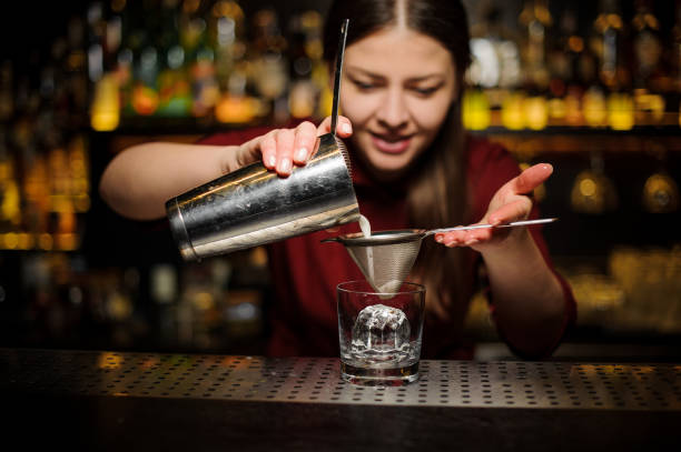 istock Female bartender pouring out a cocktail from the shaker through the sieve 939693654