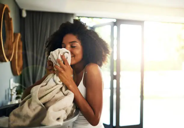 Cropped shot of an attractive young woman smelling clean laundry at home