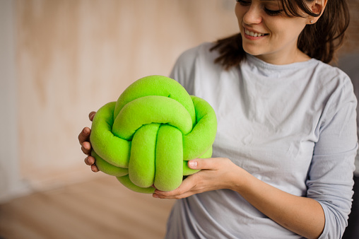 Woman in a grey shirt holding a cute green knot pillow on the indoors background