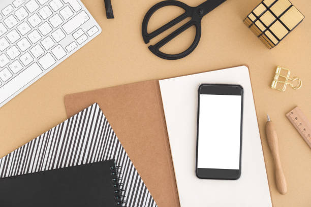 istock Beige bloggers desk, table with smartphone screen isolated , blank notebook, computer keyboard and other office supplies. Top view with copy space, flat lay. 939705780