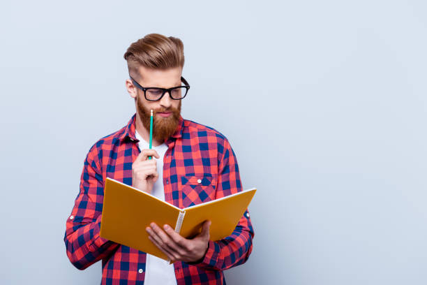 istock So nerd and stylish. Young red bearded handsome student is concentrated on studying. He is in a casual colorful outfit on pure background 939710468