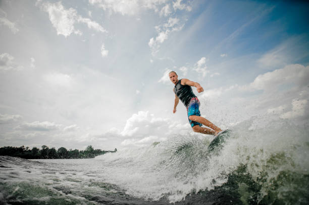 istock Athletic man wakesurfing on the board down the river against the sky 939720992