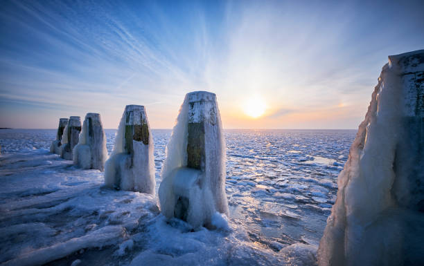 In the early morning at a frozen lake during sunrise. The poles are covered with ice due to the water which had been blown on the poles by wind force before the lake was frozen.