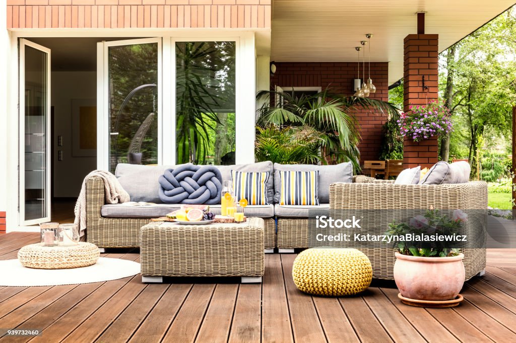 Beige garden furniture on terrace Beige garden furniture with striped pillows on wooden terrace with pink flowers and poufs Patio Stock Photo