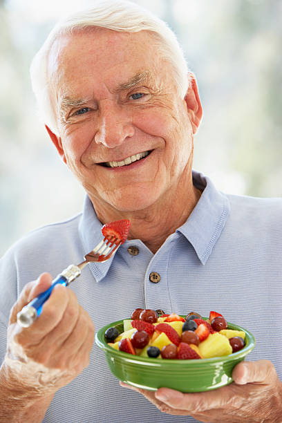 senior hombre comiendo ensalada de frutas frescas - fruit salad freshness strawberry fotografías e imágenes de stock