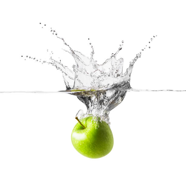 A single fresh green apple is falling into crystal clear water. Splashes of water rise high into the air above the apple, which is plunging below the waters surface. There is a clipping path around the apple and the water.