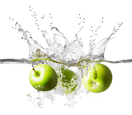 Three fresh green apples are falling into crystal clear water. Splashes of water rise high into the air above the apples, which are plunging below the waters surface. The background is white and there is a clipping path around the fruit and water.