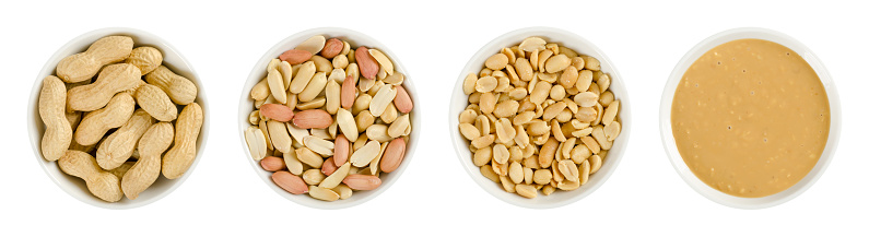Peanuts in white porcelain bowls. Roasted groundnuts in shells, shelled, salted and crunchy peanut butter. Snack and spread. Arachis hypogaea. Food photo close up from above on white background.