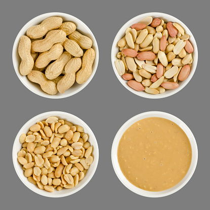 Peanuts in white porcelain bowls. Roasted groundnuts in shells, shelled, salted and crunchy peanut butter. Snack and spread. Arachis hypogaea. Food photo close up from above on gray background.