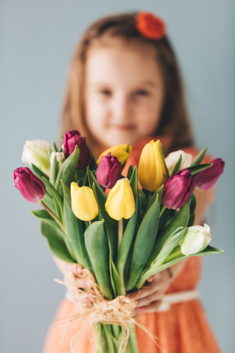 Young girl holding a bunch of colorful tulips. Mother's day gift. Parents appreciation.