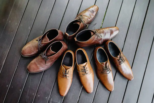 The four pairs of leather brown shoes of the groom and the bestman during getting ready for the wedding ceremony on the black wooden floor