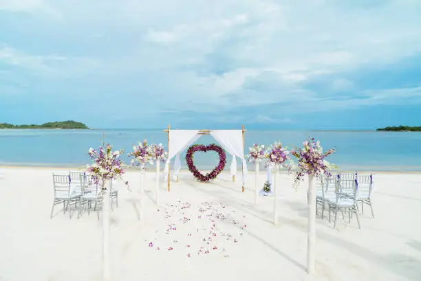 The beach weding venue setup on white sand for small size wedding ceremony with ocean view. The flowers, floral decoration with roses petals on the aisle walk way.