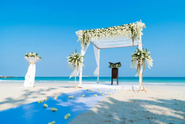 The wedding venue preparation on the beach with flowers, floral decoration on arch, altar. The panoramic ocean view in background.