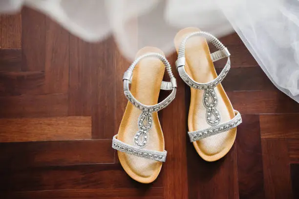 The glittering shoes of the bride from top view on the wooden floor with part of the wedding dress blurry in foreground.