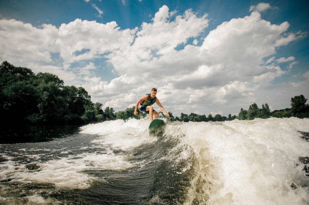 surfista caucasico a cavallo wakeboard sullo sfondo del paesaggio acquatico - wakeboarding foto e immagini stock