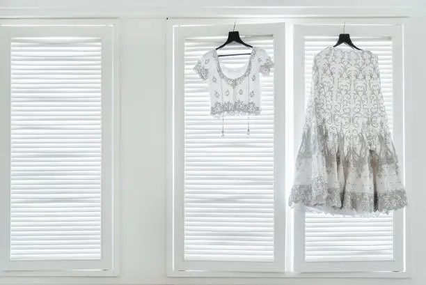 The indian wedding dress, saree and blouse hanging on the white windows with light in background.