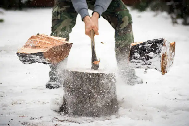 The lumberjack is cutting wood in snow while falling snow at winter.