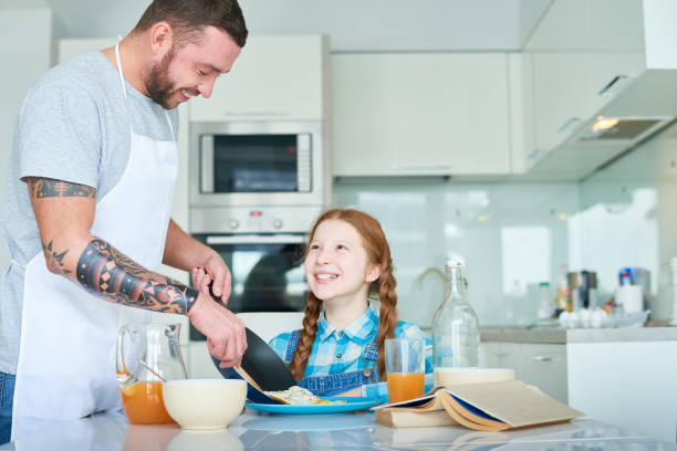 istock Happy father putting fried eggs in daughters plate 939771950