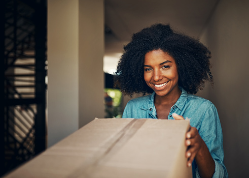 Portrait of a cheerful young woman receiving a box while standing alone at home during the day