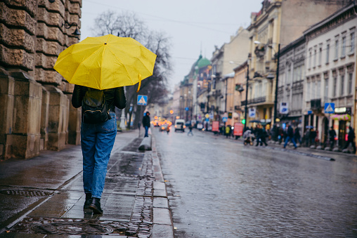 woman walk by side walk with yellow umbrella. rainy weather in old european city