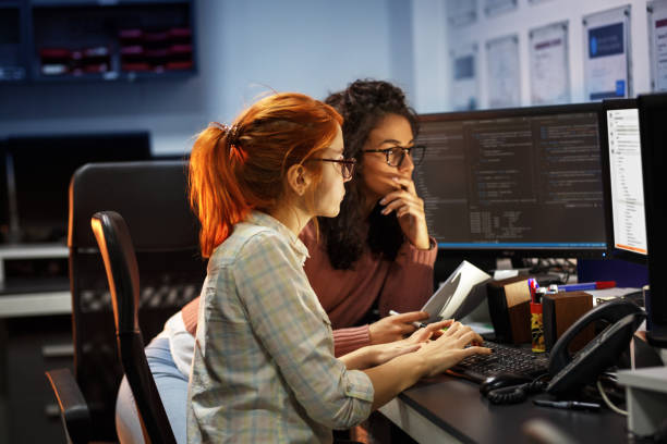 2 女性のプログラマは、新しいプロジェクトに取り組んでいます。彼らは事務所で夜遅くまで働きます。 - プログラマー ストックフォトと画像