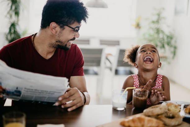 Little girl bursts into laugh while having breakfast with her father Little girl bursts into laugh while having breakfast with her father children laughing stock pictures, royalty-free photos & images