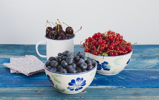 Cranberries and currants in bowl on blue wooden background.