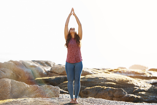 Shot of a young woman practicing the upward salute pose during a yoga routine at the beach