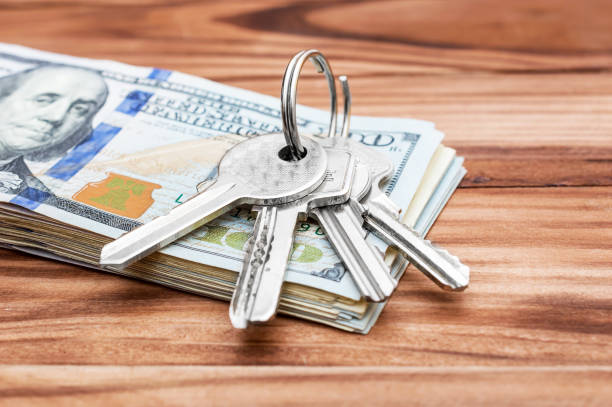 istock Keys with stack of dollar bills on wooden table. 939807748