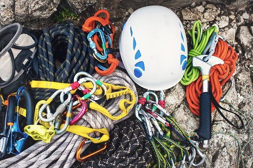 Used climbing equipment - carabiner without scratches, climbing hammer, white helmet and grey,red,green and black rope on the stone