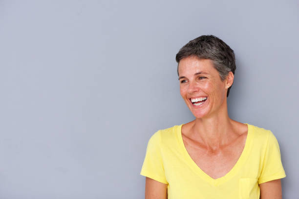istock beautiful middle age woman laughing by gray wall 939808834