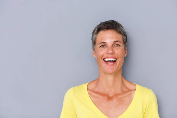 istock attractive older woman laughing by gray wall 939808838